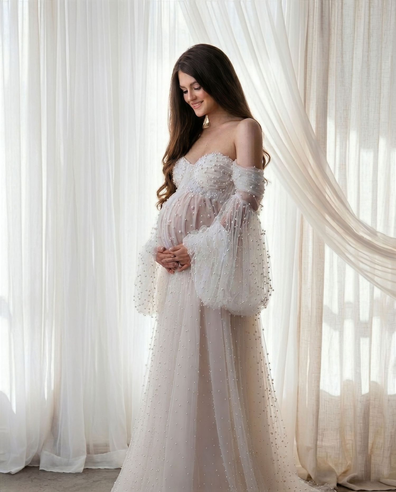 Ethereal maternity photoshoot featuring a flowing white gown and sheer robe against a light curtained backdrop.