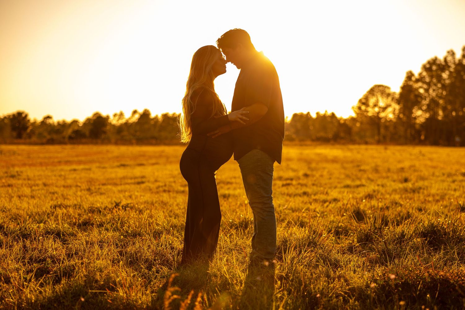 Couple embraces in field at sunset during romantic maternity photo session. Oviedo, Florida