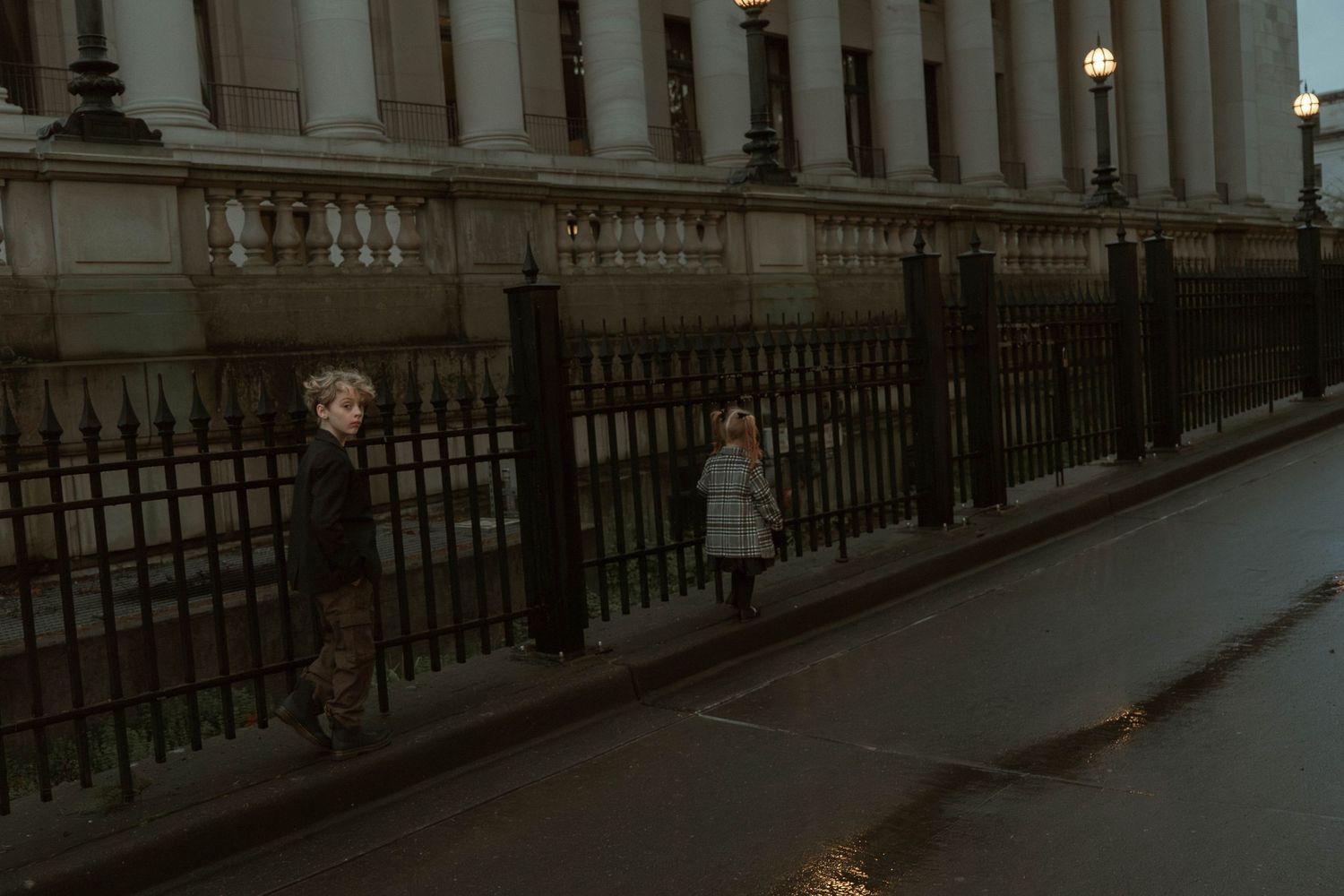 Moody vintage photograph of children playing by iron fence railings at dusk.