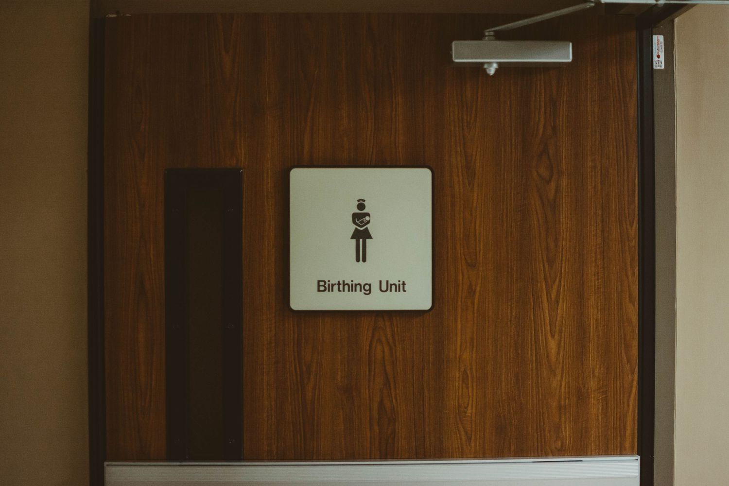 Medical equipment and wooden wall visible in a hospital birthing unit hallway.