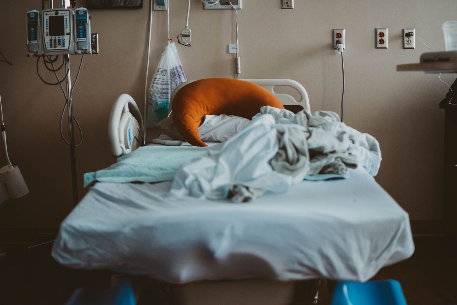 Hospital bed with white linens in dimly lit medical room.
