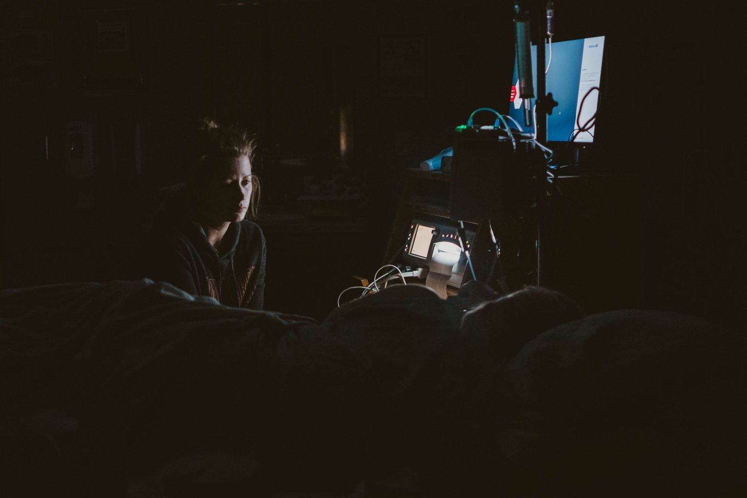 Dark hospital room with medical equipment silhouetted against window light.