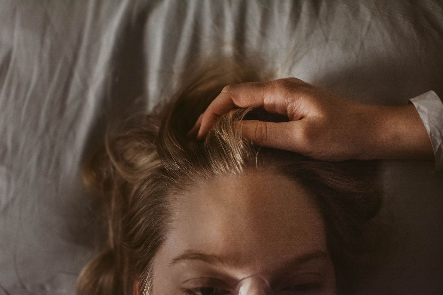 Hand gently stroking hair in intimate morning light.