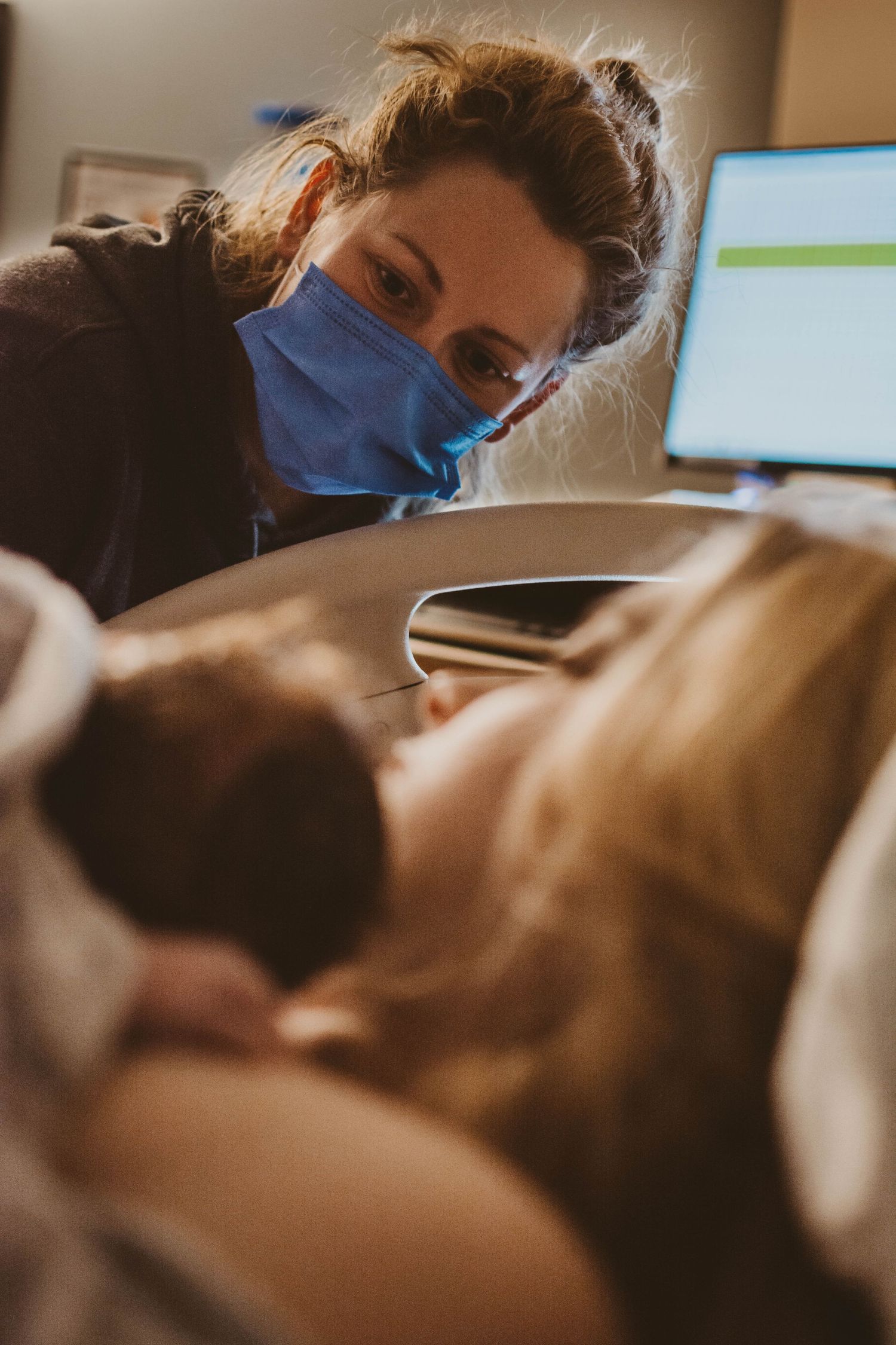 Medical professional in blue mask attending to patient in hospital bed.