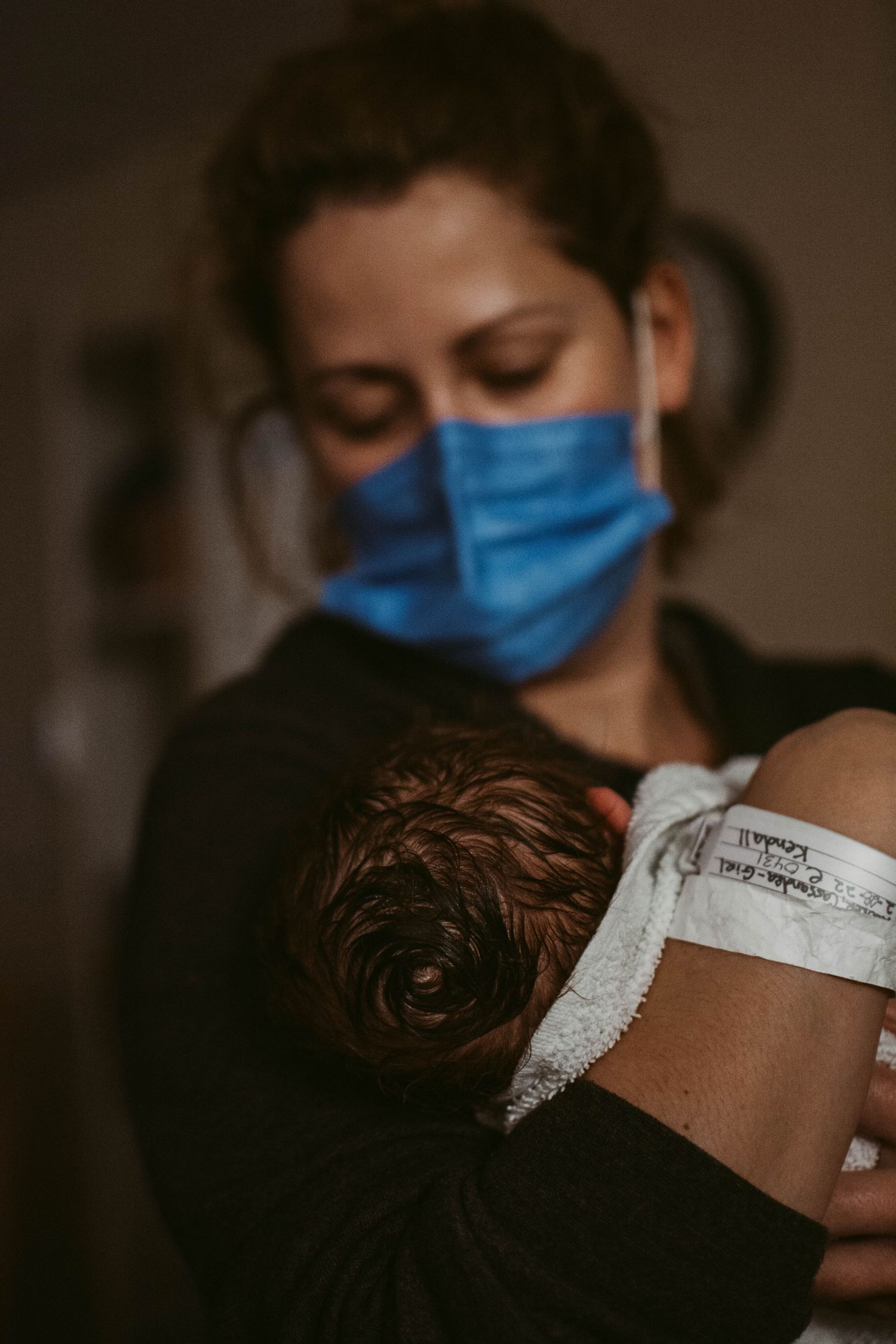 Medical professional in blue mask working in low-light hospital setting.