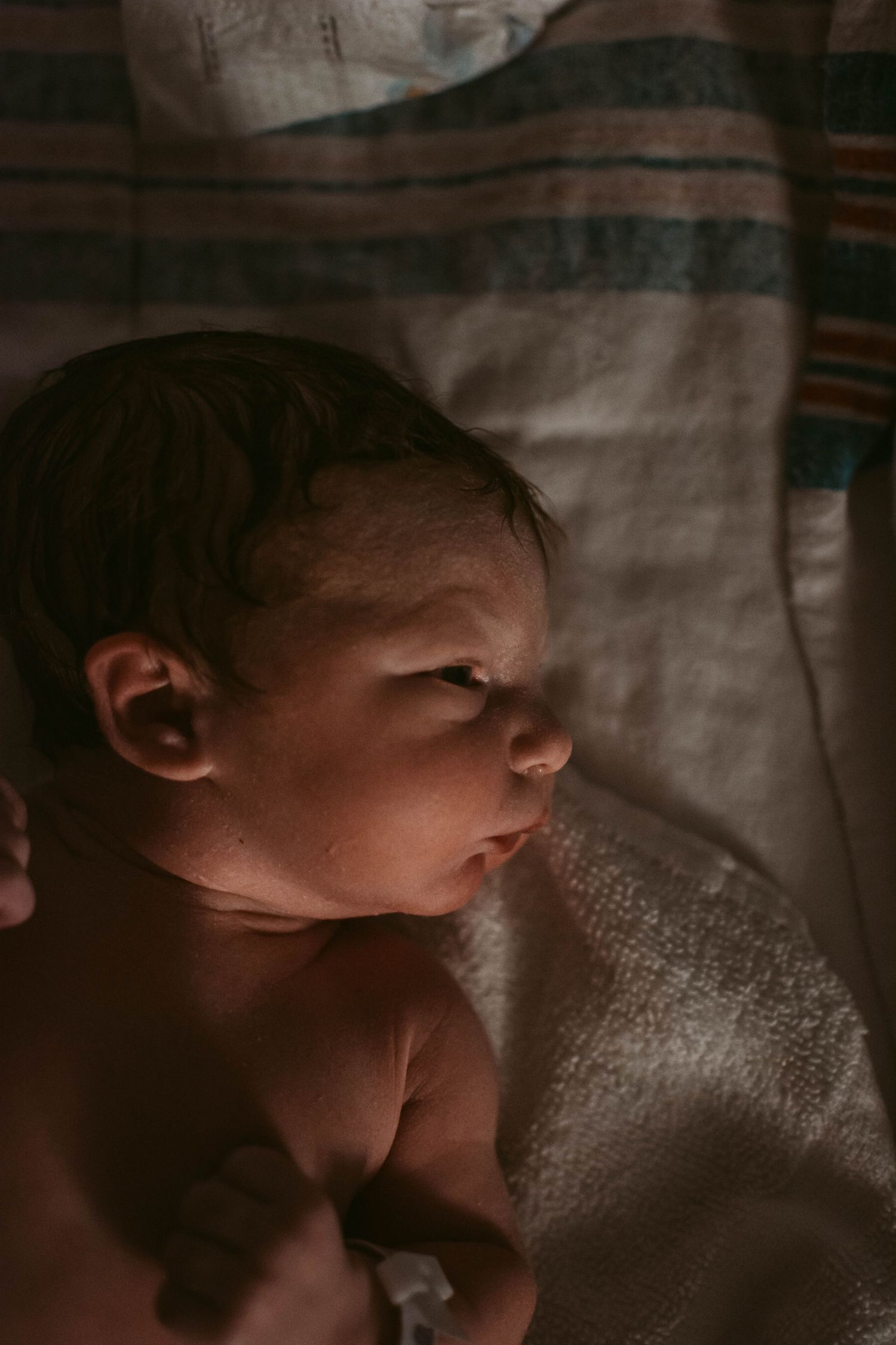Newborn infant sleeping peacefully on soft bedding in dim lighting.