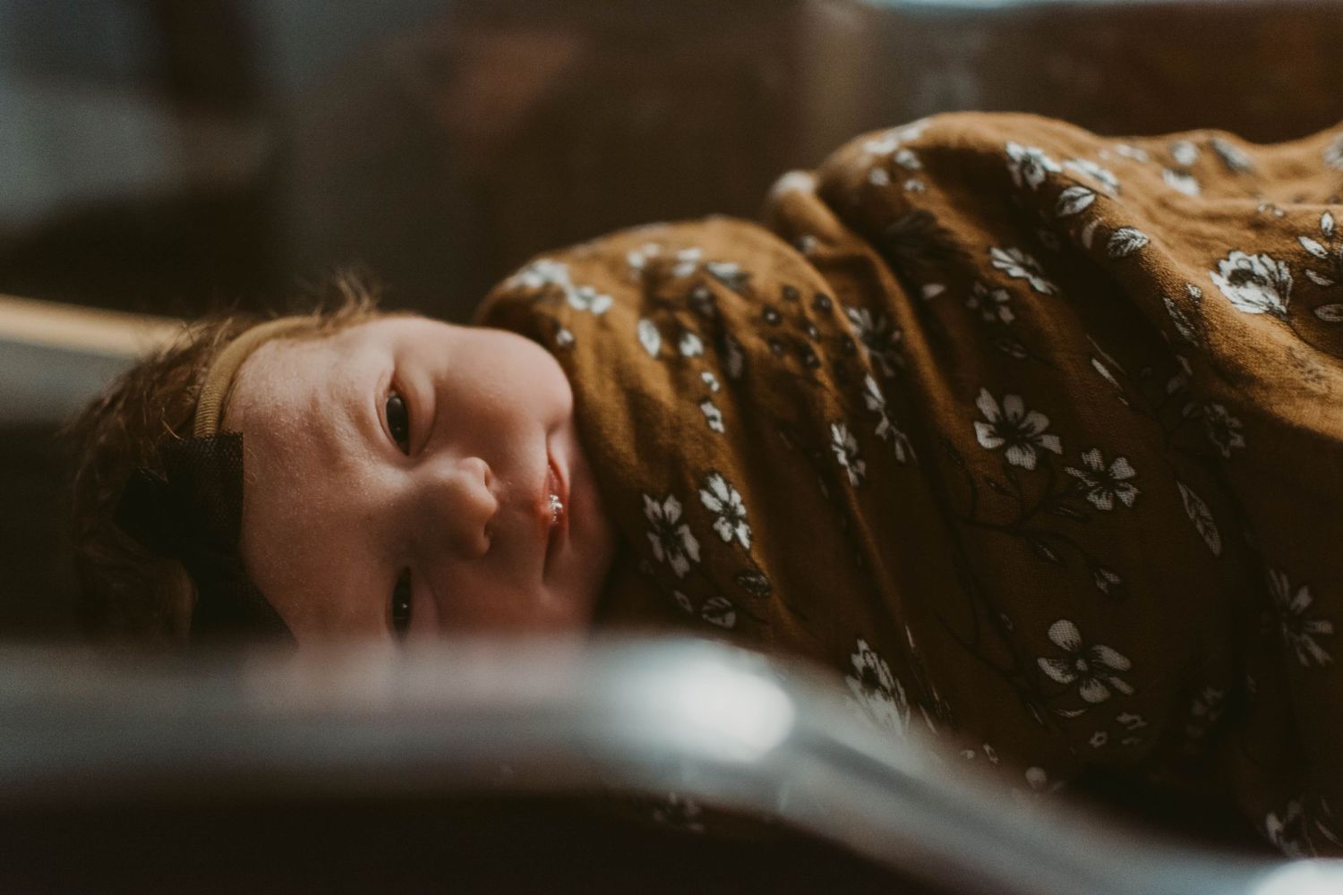 Baby resting calmly while swaddled in brown floral blanket.