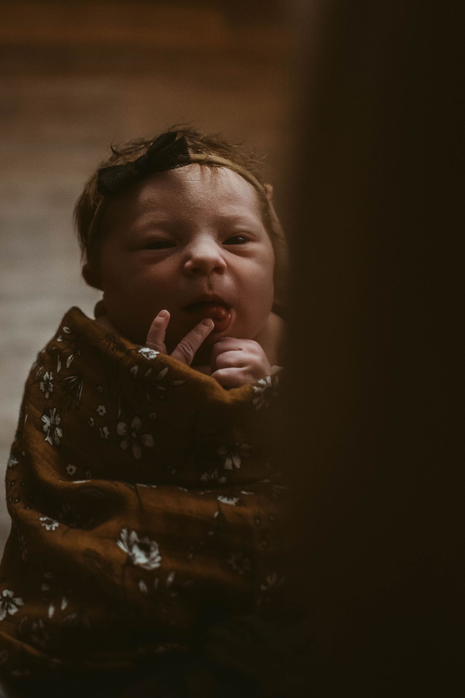 Baby wrapped in brown floral swaddle with playful expression.