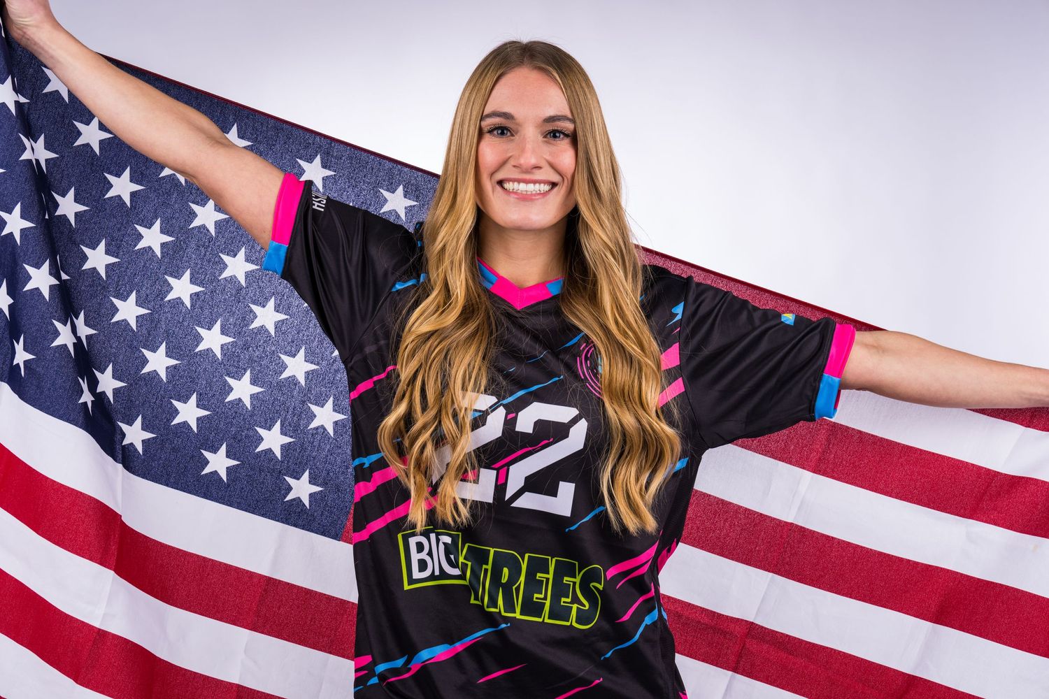A woman from the Snohomish Sky women's indoor soccer team is posing with the American flag draped on her back.
