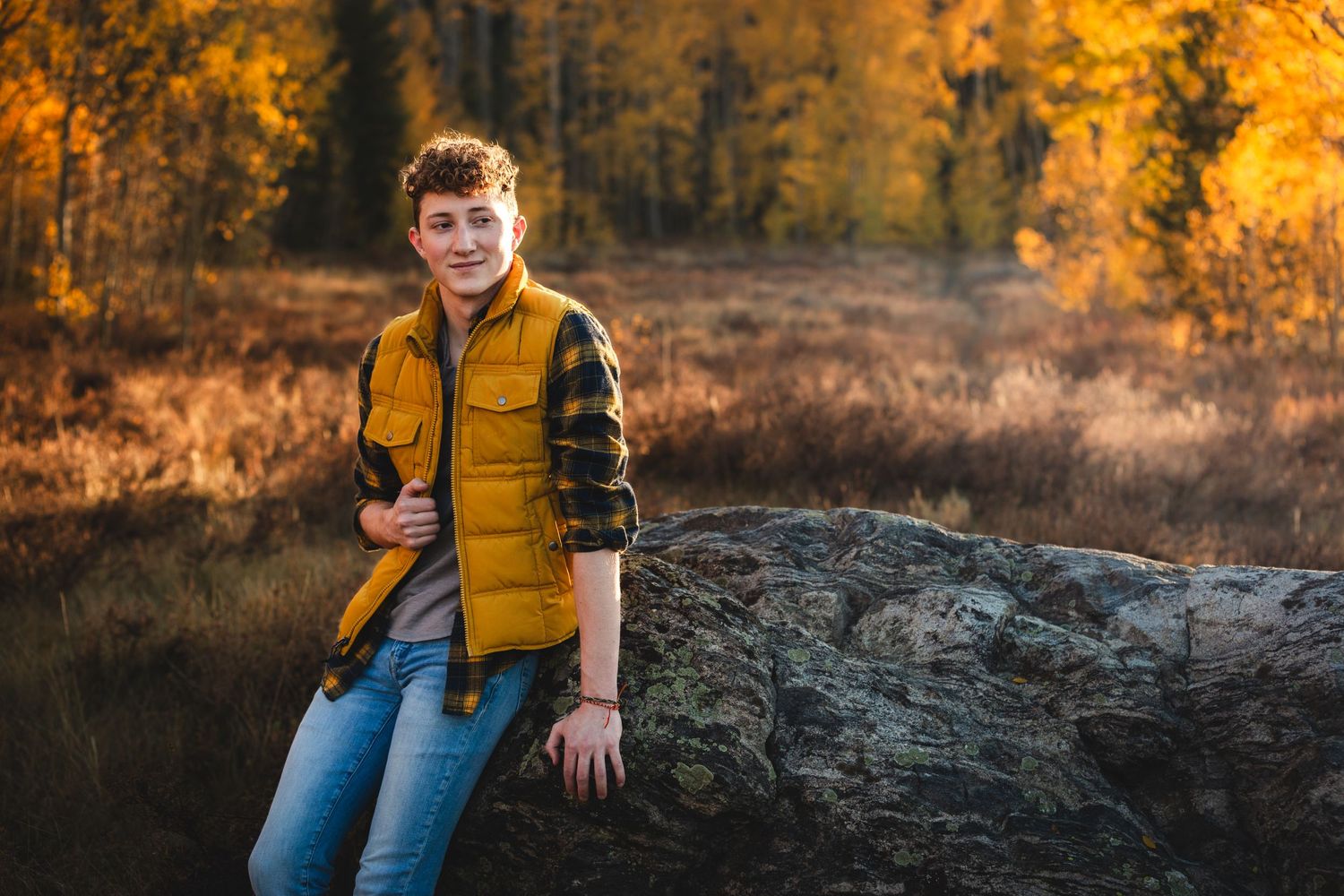 Person in yellow vest sits on large rock during autumn with orange foliage in background, in Frisco, Colorado - Senior Photos