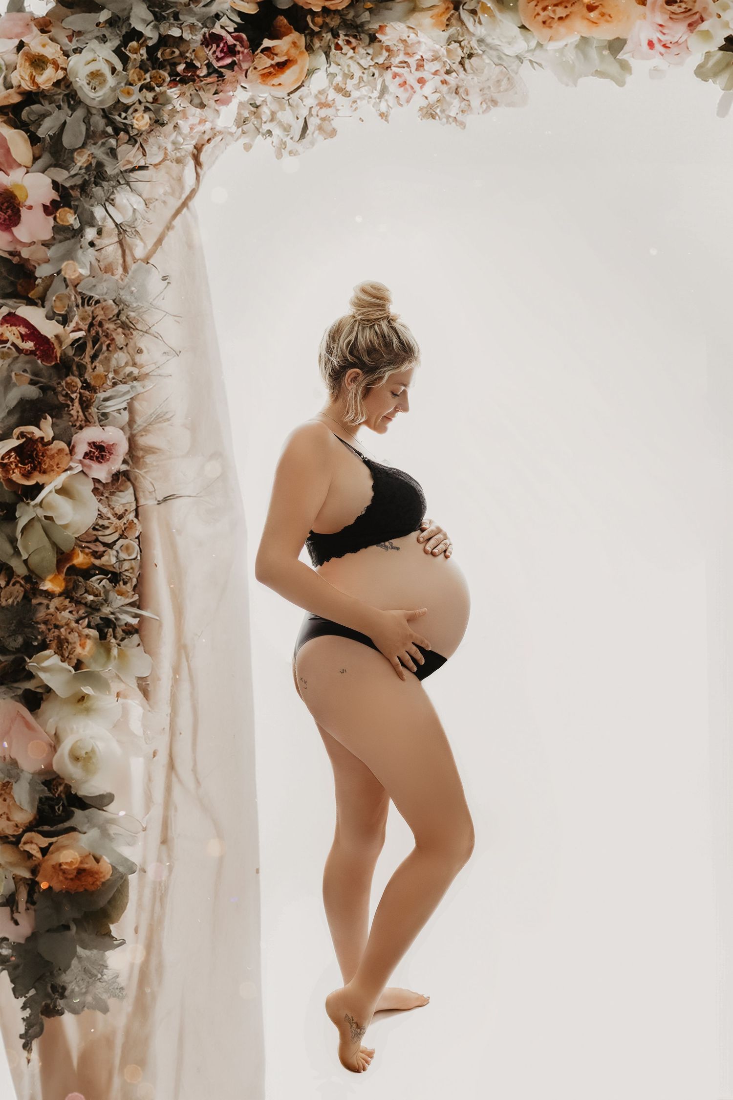 Artistic maternity silhouette against white background with floral arch decoration.