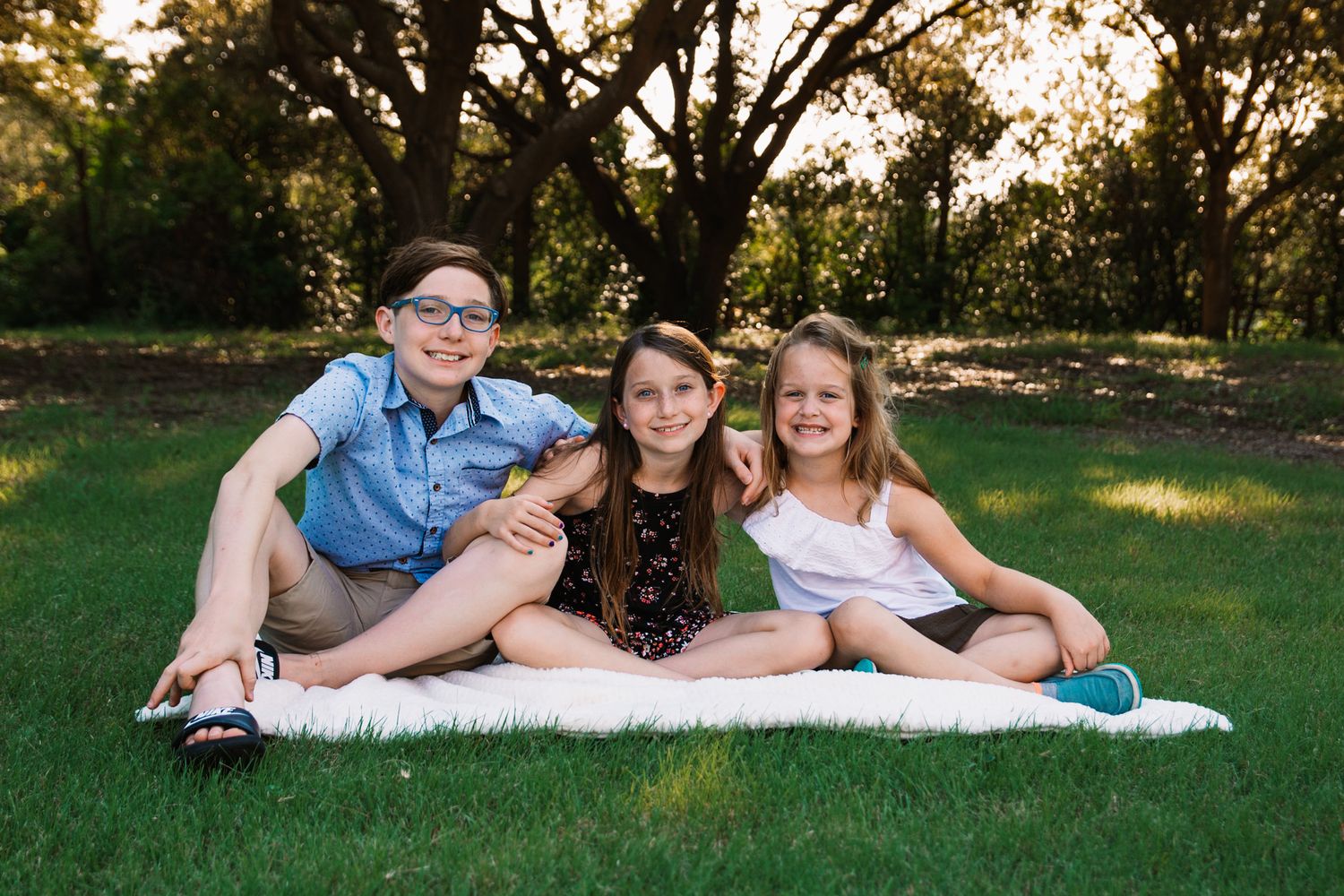 3 school aged kids posing together on blanket in park during family photo session by mesquite, tx family photographer