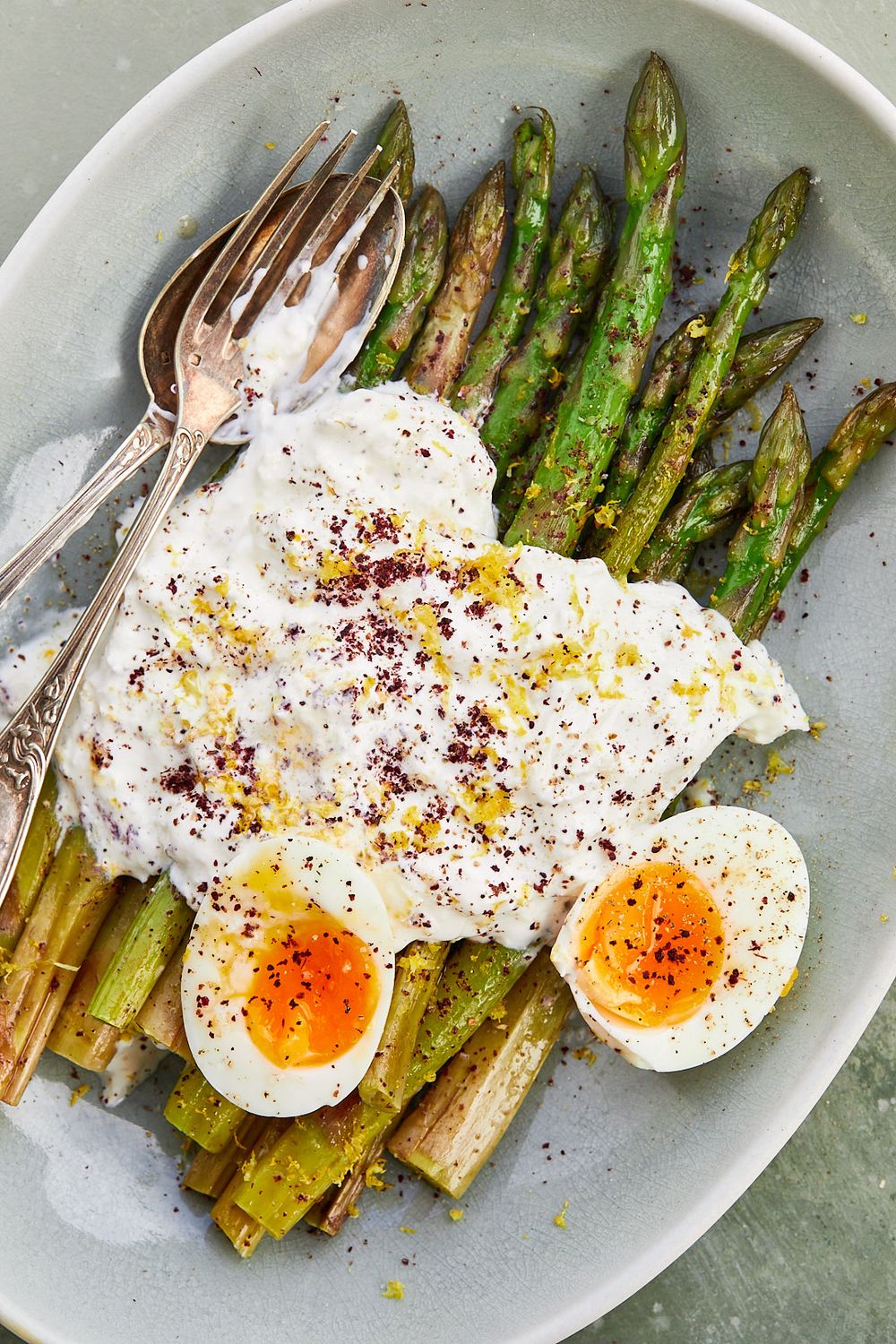 Roasted asparagus spears with soft boiled eggs and seasonings on a white plate.
