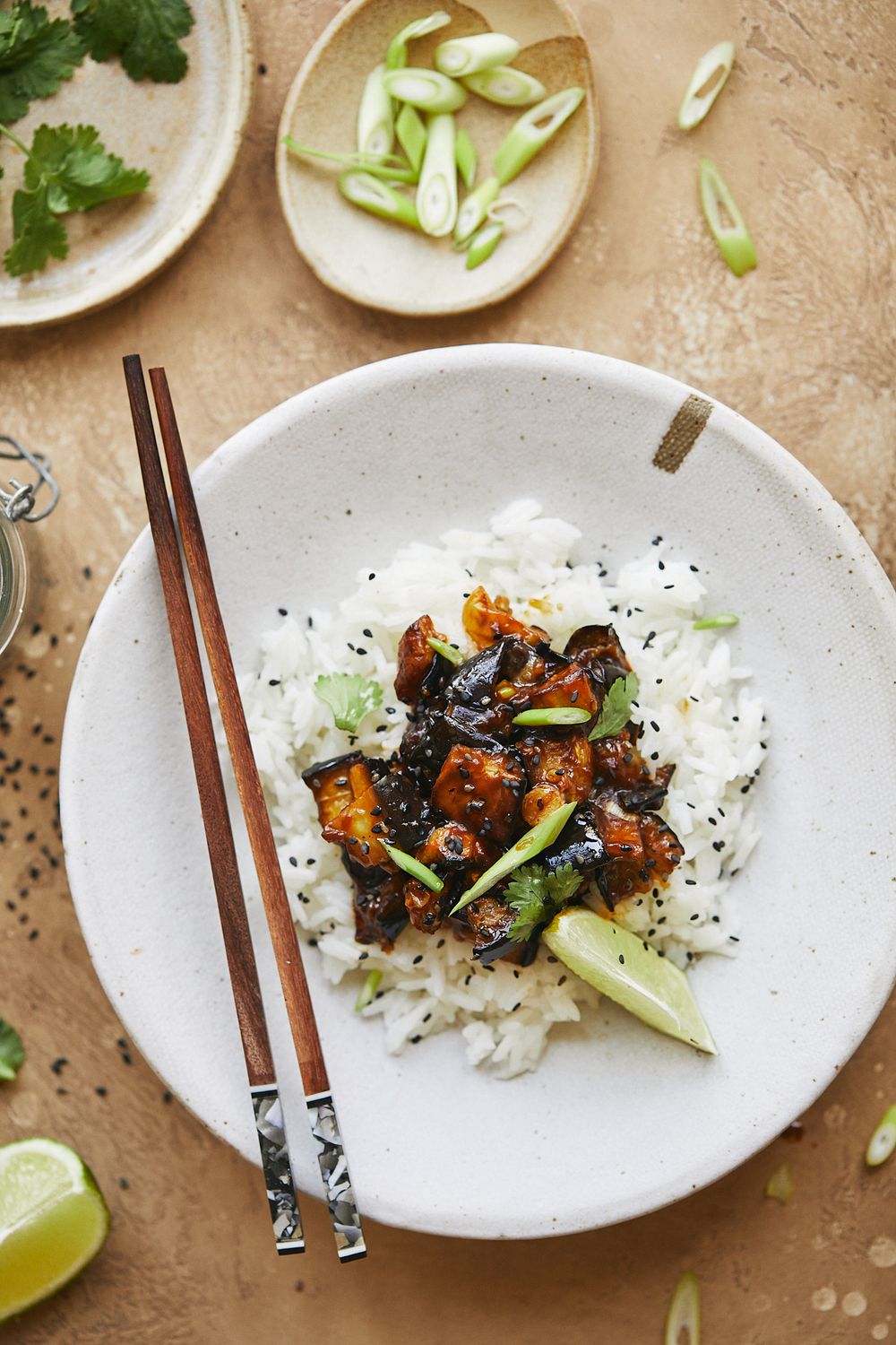 Asian-style rice bowl with glazed tofu, green onions, and chopsticks.