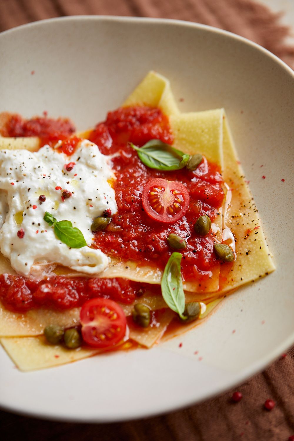 Fresh pasta with tomato sauce, burrata cheese, capers and basil leaves.
