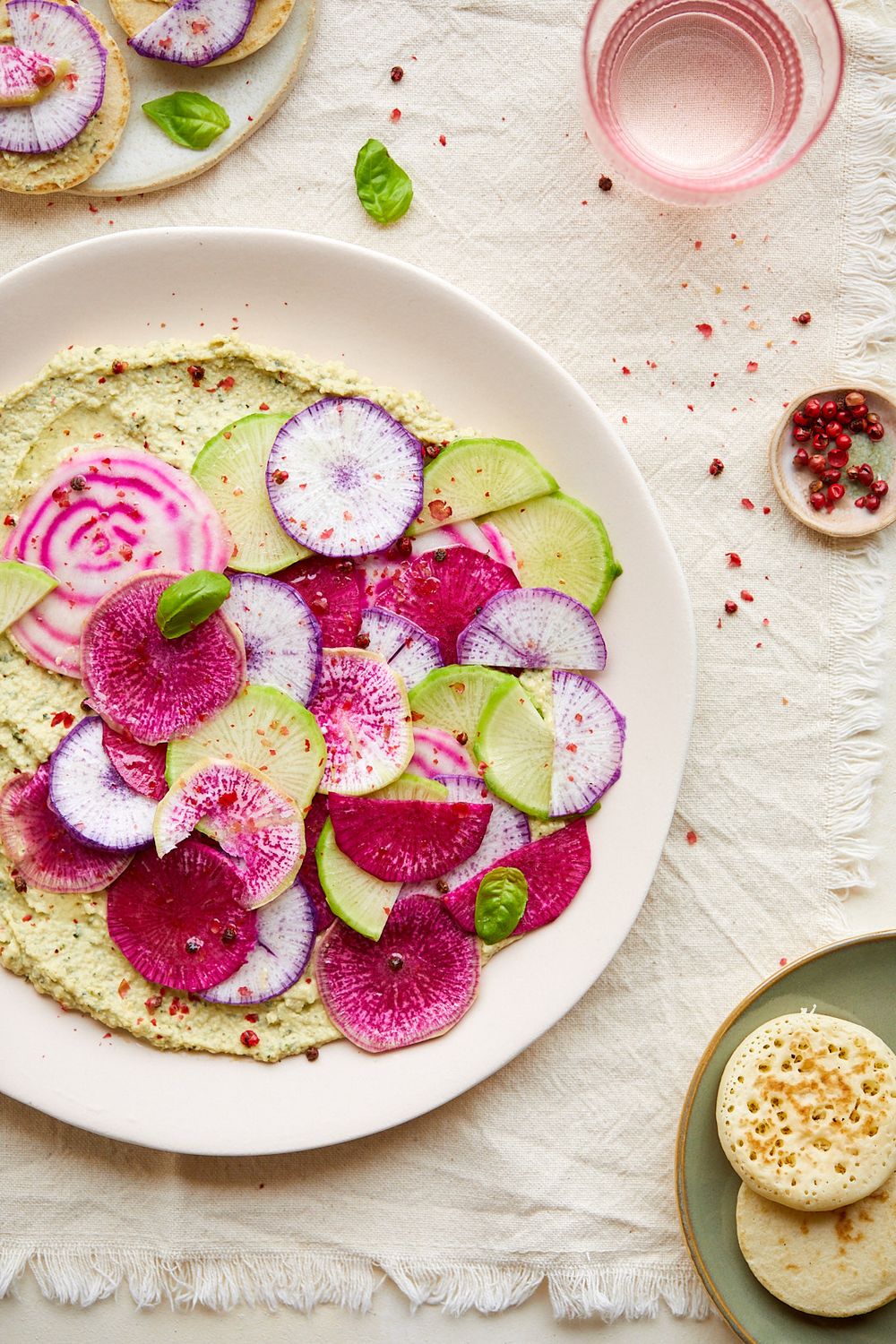 Colorful plate with sliced watermelon radishes and avocado on white linen tablecloth.