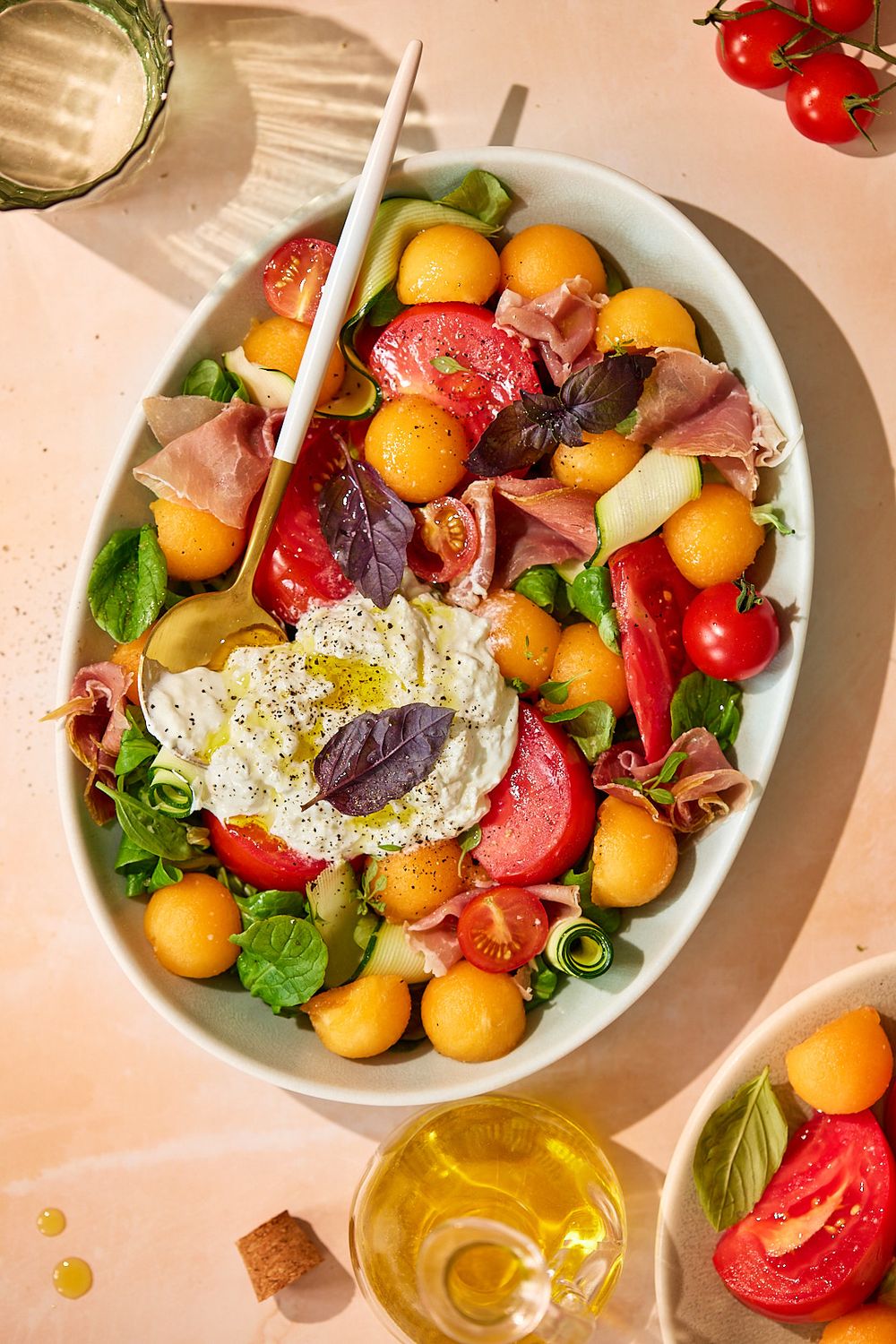 Colorful melon salad with prosciutto, fresh tomatoes, and burrata cheese drizzled with olive oil.