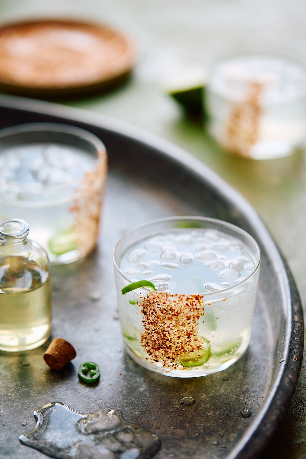 Craft cocktail with sesame rim garnish and lime wedge served on a metal tray with ice.