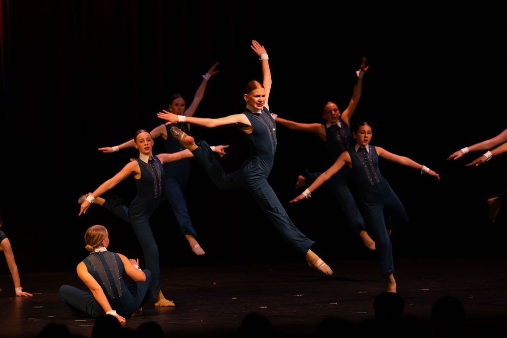 Silhouetted dancers perform a dynamic piece on stage with outstretched arms and elegant poses in the darkness.