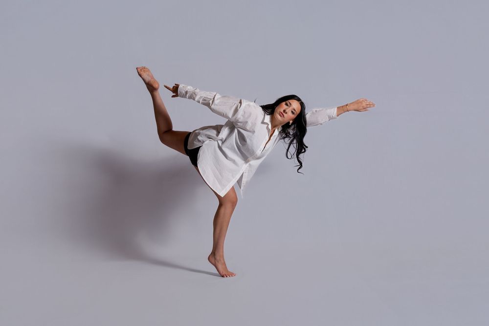 Athletic person performs a high side kick wearing a white martial arts uniform against a gray studio background.
