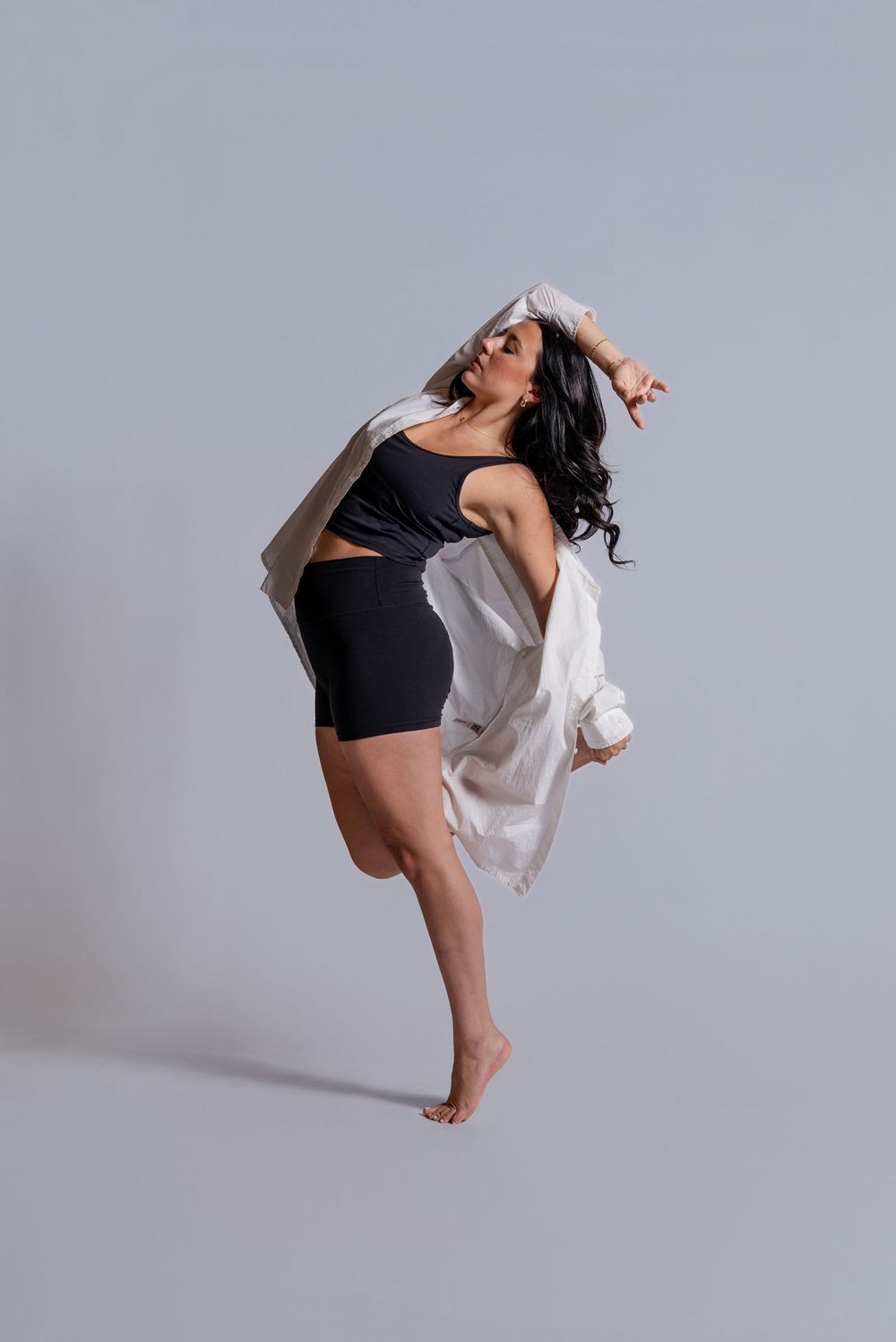 A contemporary dancer in black and white attire performs a dramatic leap sequence against a light gray studio background.