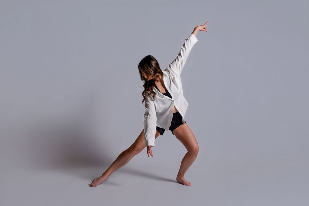 Athletic dancer in white jacket and black shorts strikes dynamic pose against gray background during performance.