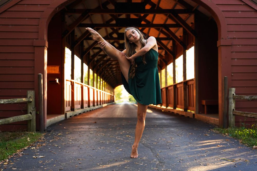 Elegant dance movements performed in sunlit covered bridge passageway.