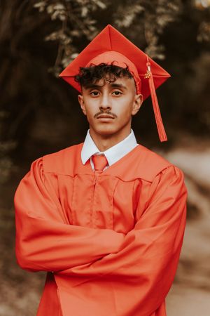 Graduate in bright red cap and gown poses for portraits outdoors.