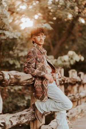 Graduate in casual attire poses on rustic fence during golden hour photoshoot.