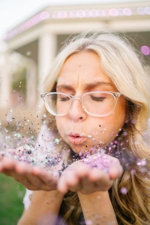 Close-up of person blowing sparkly glitter with playful expression.
