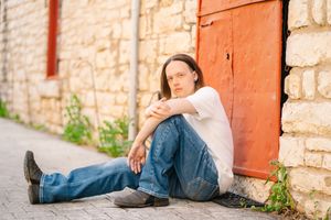Person in casual attire relaxing against rustic stone wall outdoors.