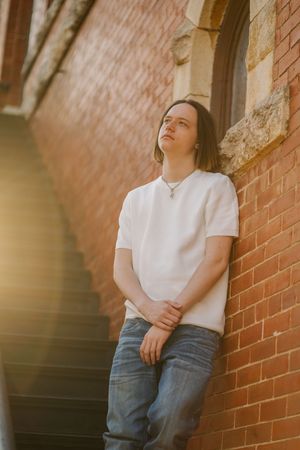 Candid portrait against brick wall wearing white t-shirt and jeans in natural lighting.