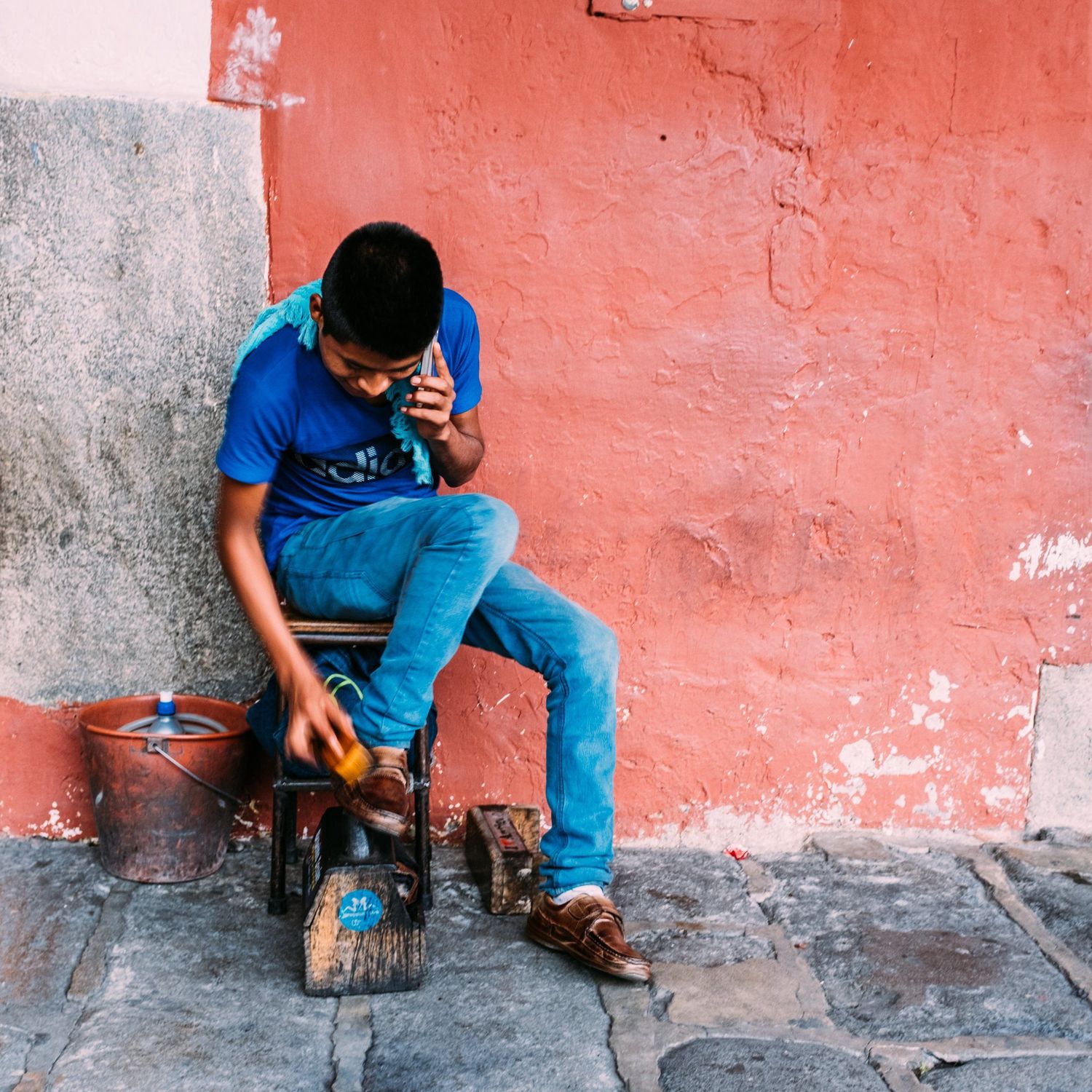 A person in blue sits against a coral-colored wall examining an object.