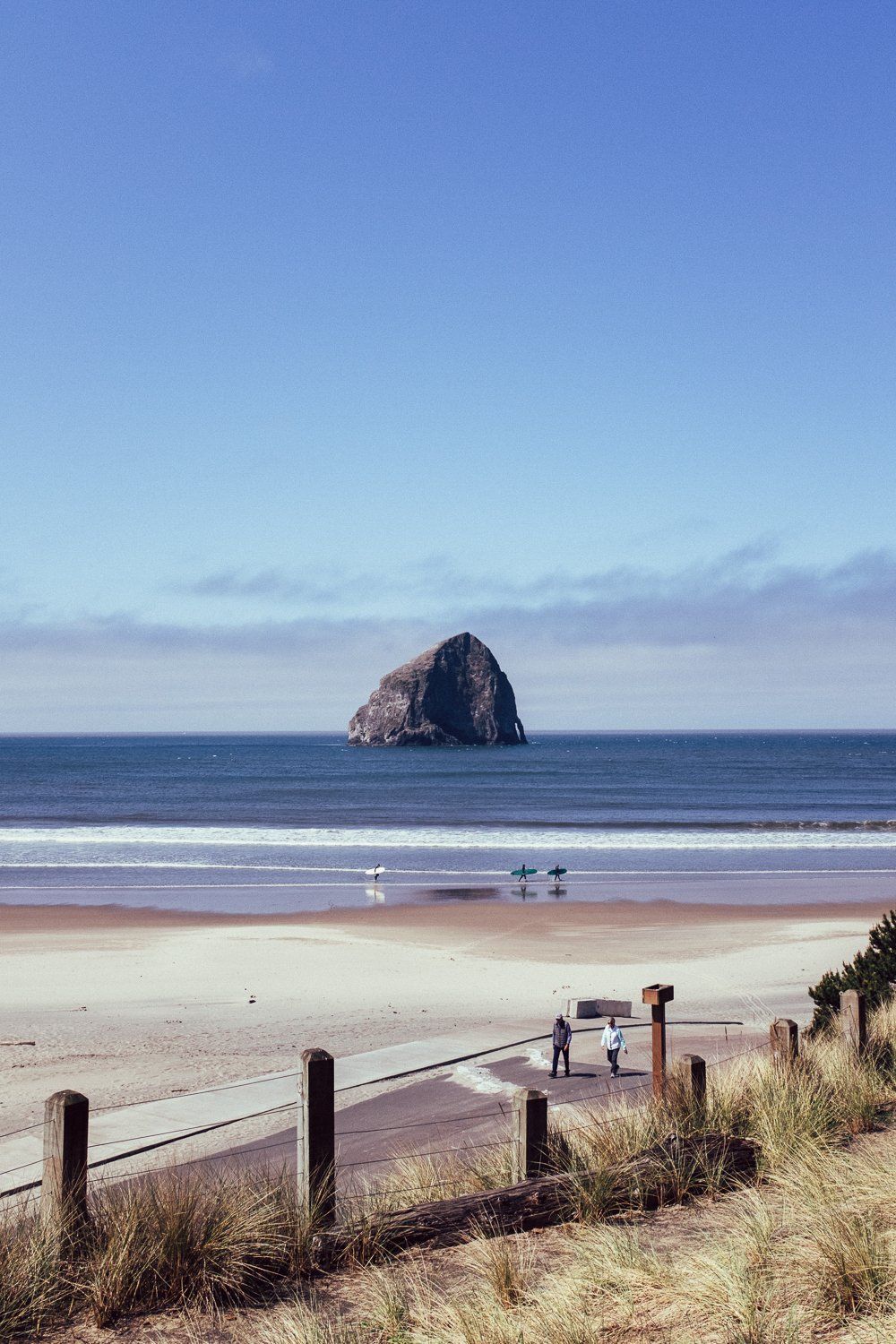 Famous Haystack Rock rises from the ocean at Pacific City beach with people walking on the shore.