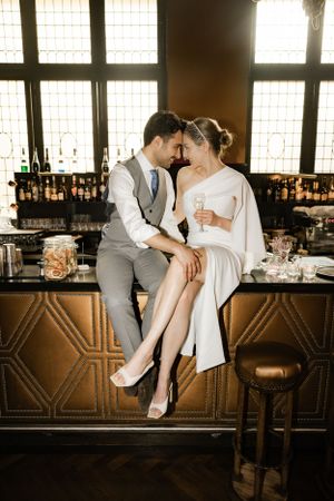 Couple sitting at an art deco style bar in formal wedding attire.