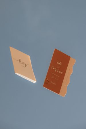 Brown and beige wedding invitation cards floating against a blue background in a creative sequence.