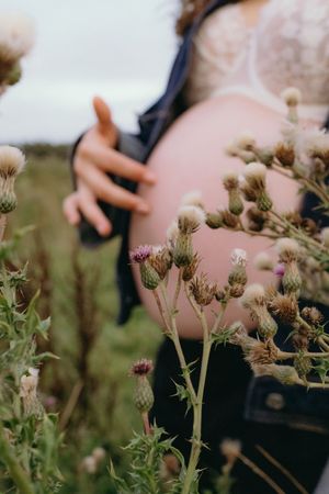 Artistic detail shot of wildflowers in foreground with maternity silhouette in background.