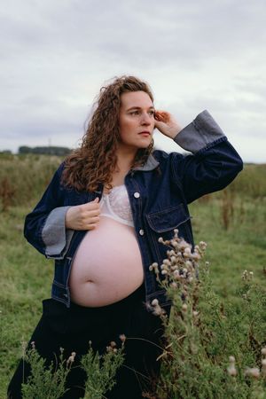 Artistic maternity portrait in a wildflower field with moody overcast sky.