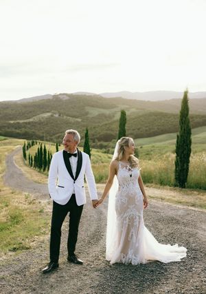 Wedding couple walking along a scenic Tuscan road lined with cypress trees at sunset.