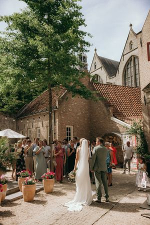 Wedding guests gathered in courtyard of historic brick building during daytime celebration.