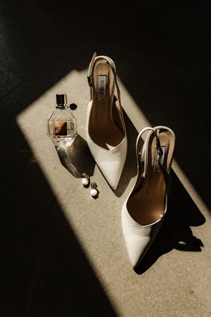 White bridal heels and perfume bottle arranged in dramatic lighting and shadows.