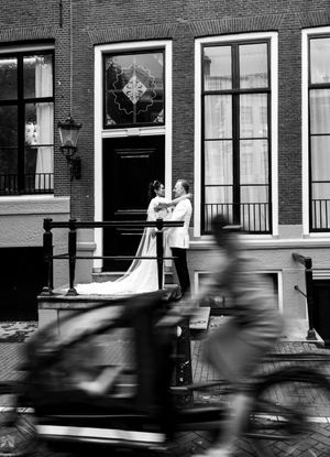 Black and white street scene with motion blur of passing cars in front of brick buildings.