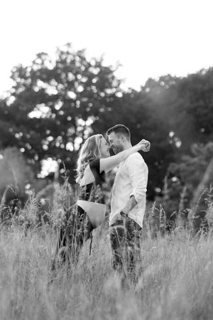 Romantic couple embracing in a tall grass field during sunset creating a dreamy silhouette effect.
