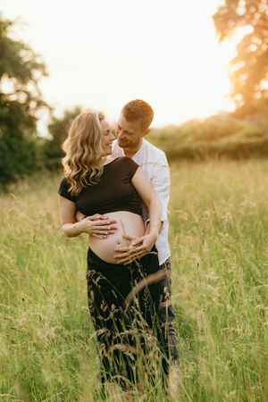 Intimate maternity photoshoot in a sun-drenched meadow with golden hour lighting.