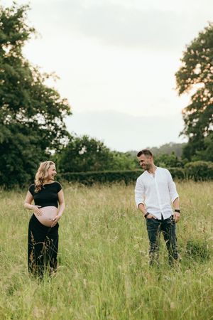 Expectant couple sharing playful moments in a rustic field setting.