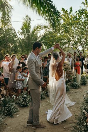 Wedding couple dancing outdoors among palm trees and tropical greenery with guests watching.