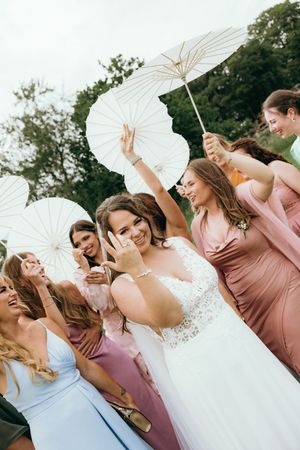 Bridal party holds white parasols while posing together outdoors in pink dresses.
