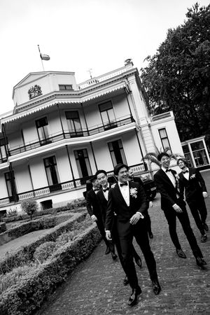 Groomsmen walking and laughing together outside a white historic building.