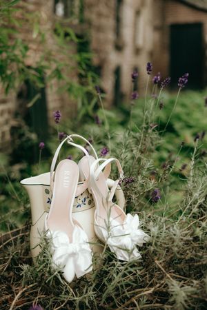 White bridal shoes with floral details placed among lavender flowers and greenery.