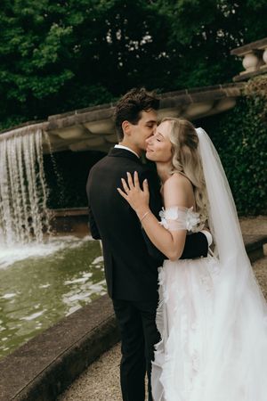 Wedding couple sharing romantic moments by outdoor waterfall feature.